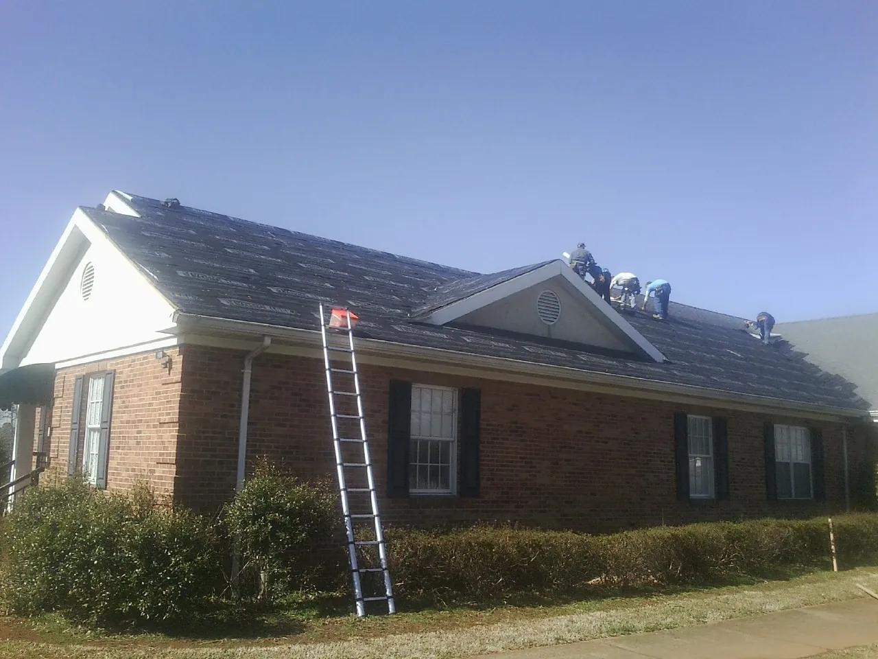 Crew tearing shingles off a brick ranch roof with a ladder set — Metal Roof Repair work by our crew in Dedham