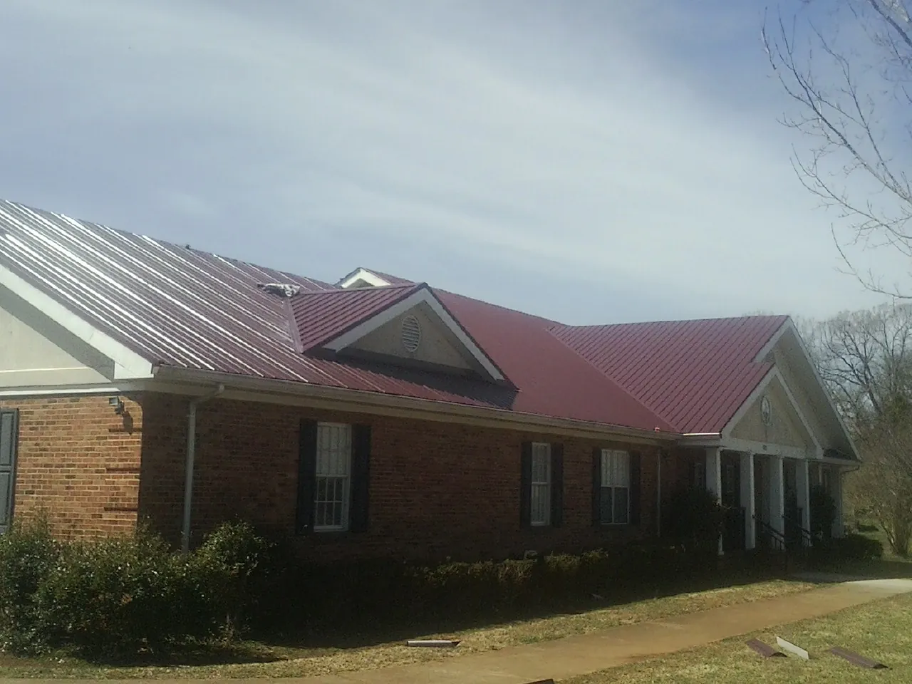 Red metal roof with gabled entries on a long brick building, from a Hail Damage Roof Repair job in Dedham