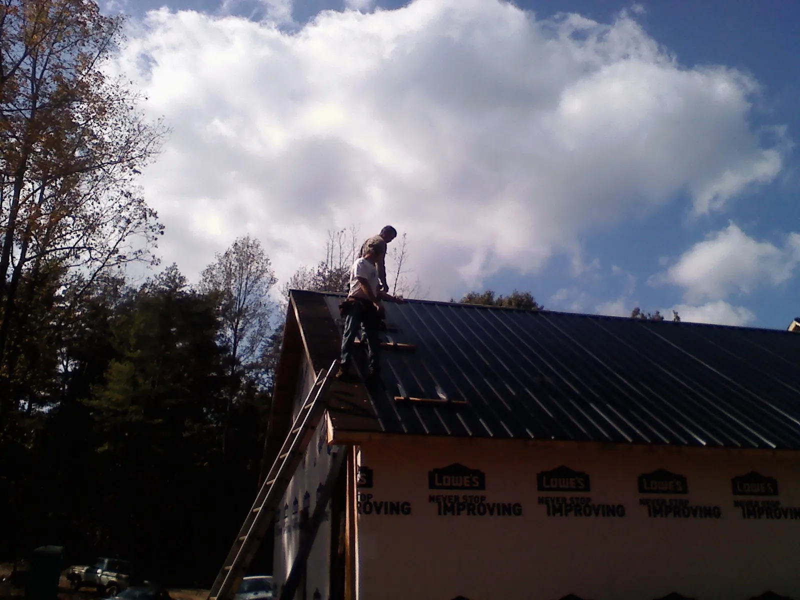 Roofer fastening dark metal panels high against a cloudy sky, from a Roof Inspection job in Dedham