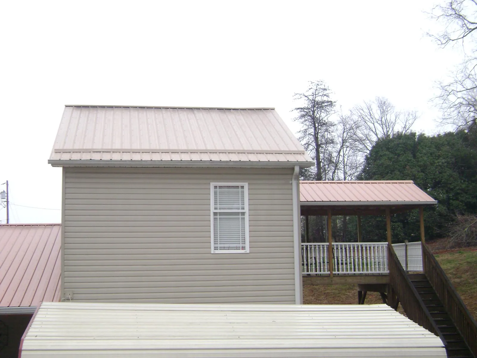 Tan metal roofs on a two story addition and attached porch, from a Roof Replacement job in Dedham